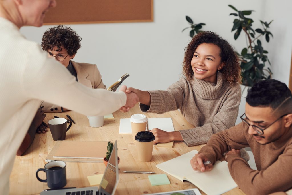 Cuatro personas en una mesa de oficina teniendo una reunión y dándose la mano para cerrar algún trato o acuerdo empresarial