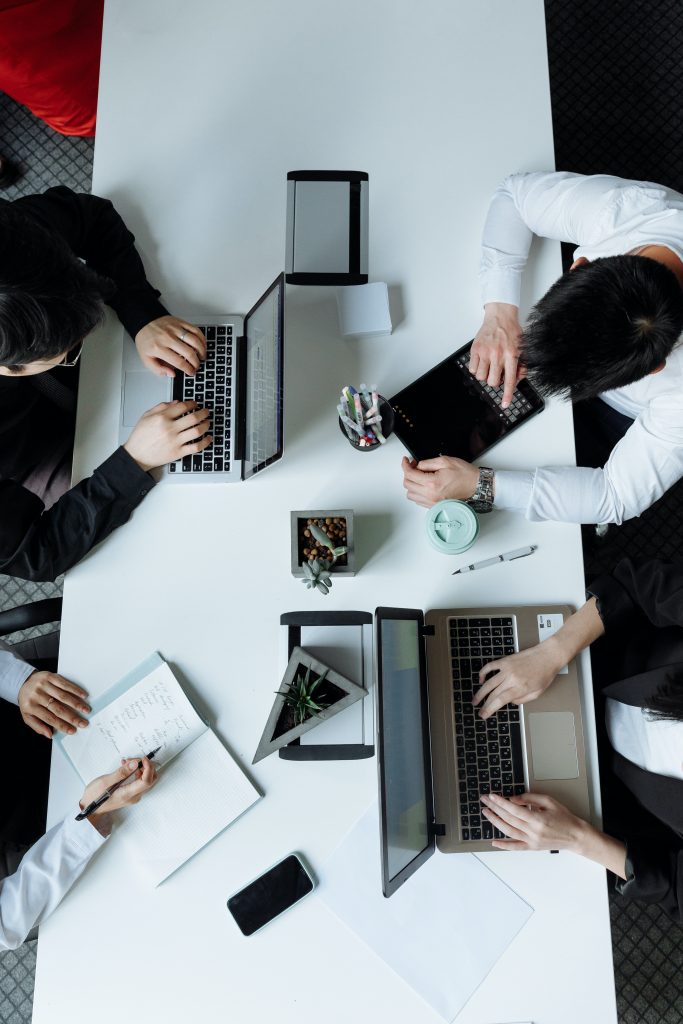 Mesa de oficina con cuatro personas trabajando, vista desde arriba, foto en color